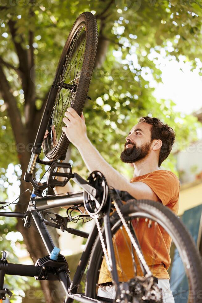 enfocado joven masculino ciclista asegura bicicleta es bien preparado para al aire libre aventuras por diligentemente asegurando neumático goma. sano y activo hombre participación bicicleta rueda para mantenimiento. foto