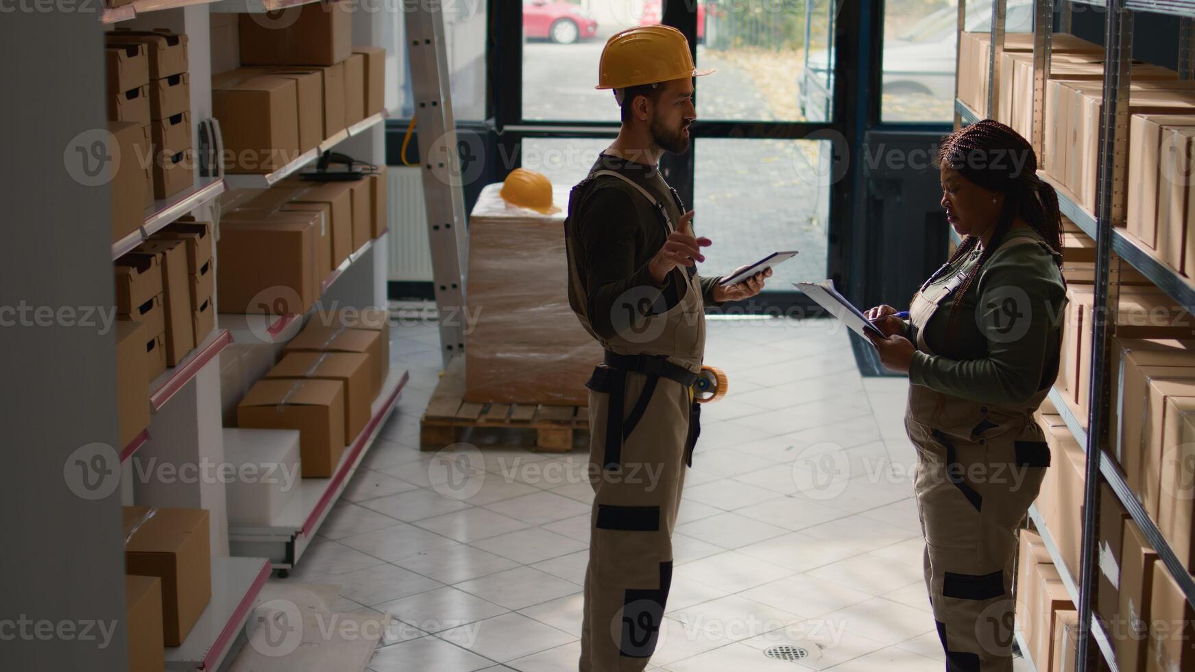 Employees in warehouse inputing updated products info on online shopping website using tablet, walking through retail stockroom aisles reviewing labels on wares, crosschecking with inventory list photo