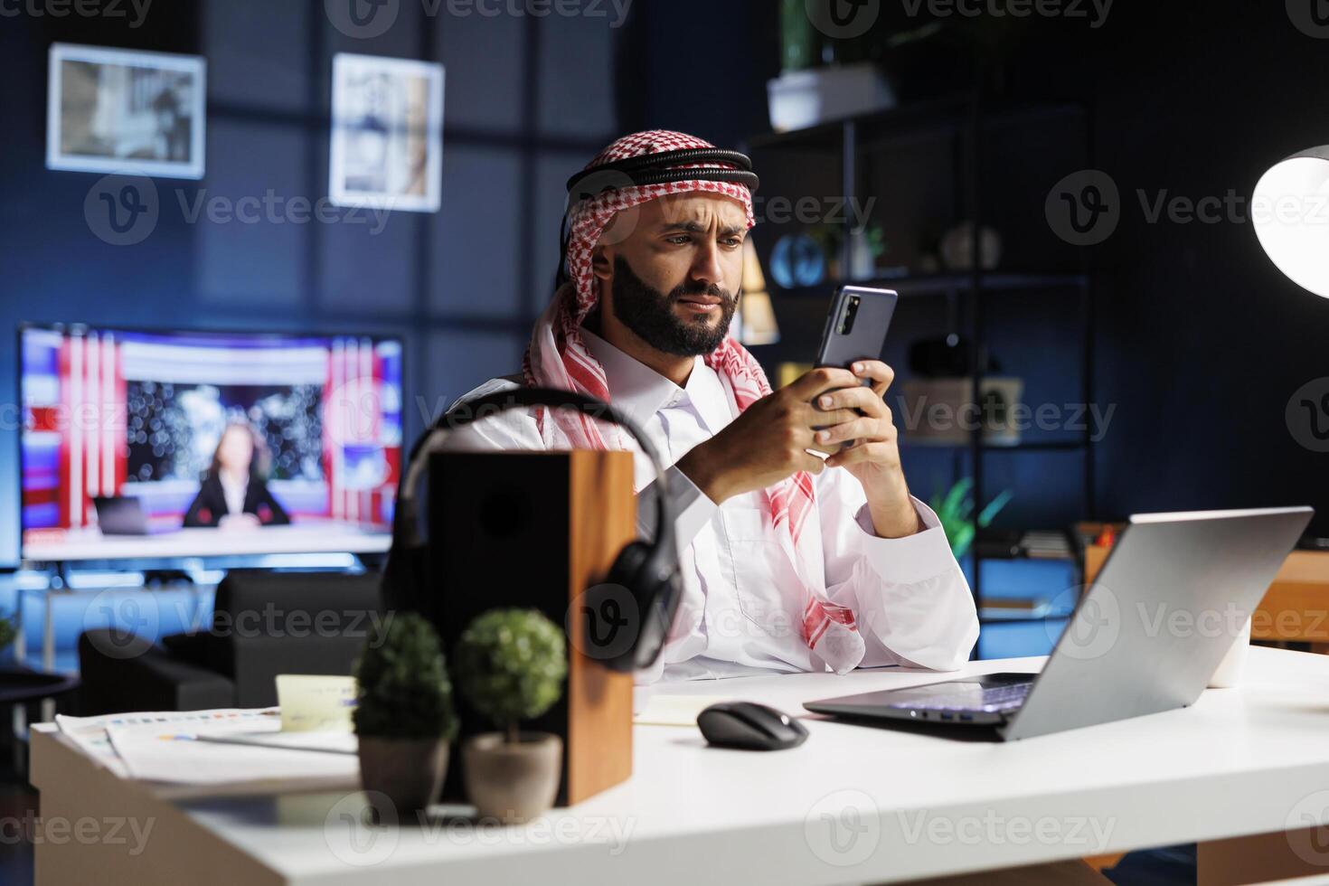 Professional Arab man works in an office, using a computer and smartphone for online research and communication. He is confident and dedicated, seamlessly combining Islamic values with technology. photo