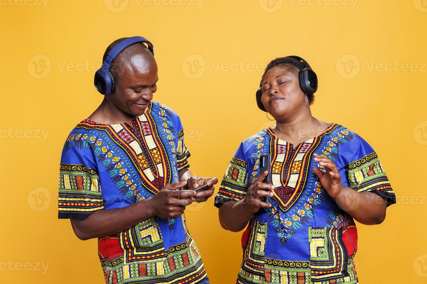African american couple enjoying music together using headphones and smartphone. Woman listening to playlist with closed eyes and satisfied expression while man turning on song on mobile phone photo