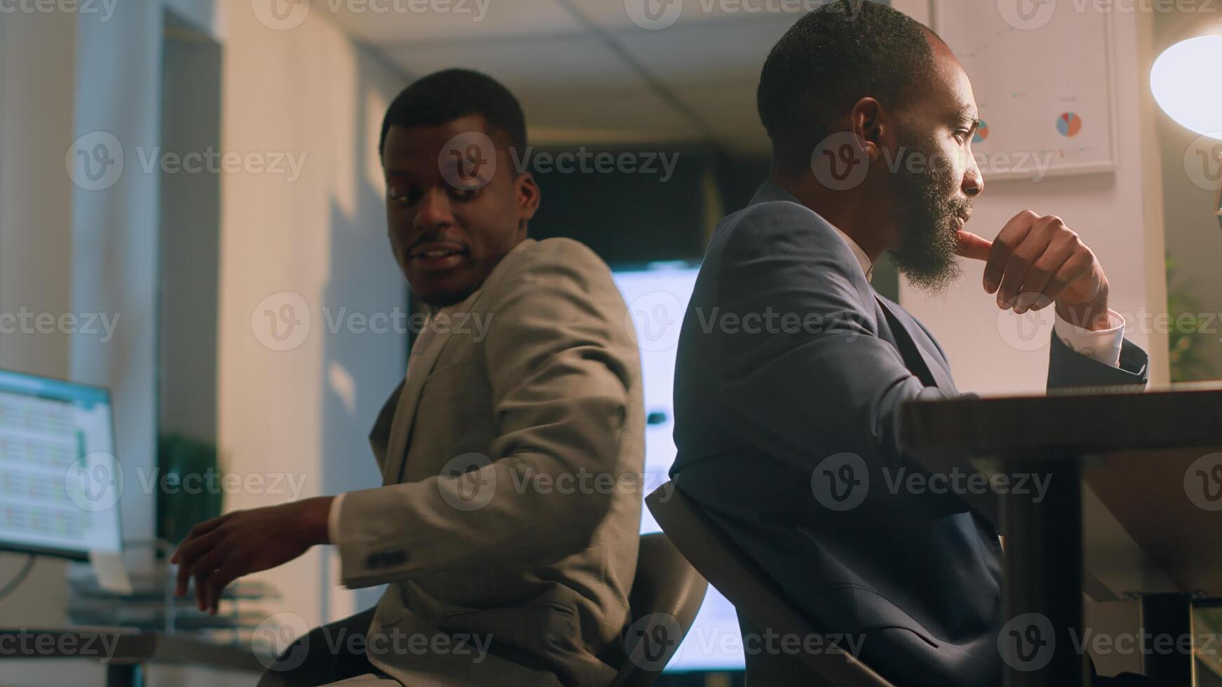 Friendly businessman having fun at work during nightshift, bumping into colleague using desk chair. Coworkers racing eachother to get out of tedious routine during overnight stay in office photo