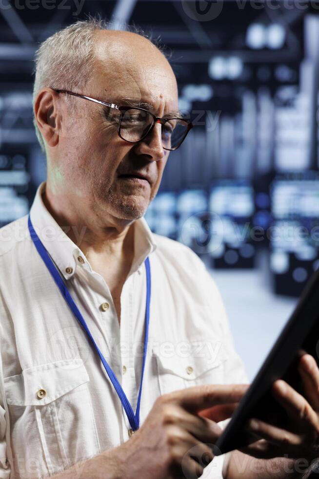 Qualified electrician in crypto mining farm with specialized electronics using Blockchain technology. Elderly wireman holding clipboard, inspecting asic server rows solving hashing operations photo