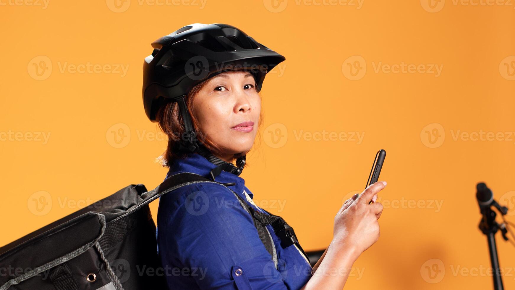 cerca arriba de mensajero mensajes de texto cliente a prisa arriba. bicicleta jinete tarde para siguiente entrega ubicación, esperando para cliente a recoger arriba comida orden, aislado terminado naranja estudio antecedentes foto