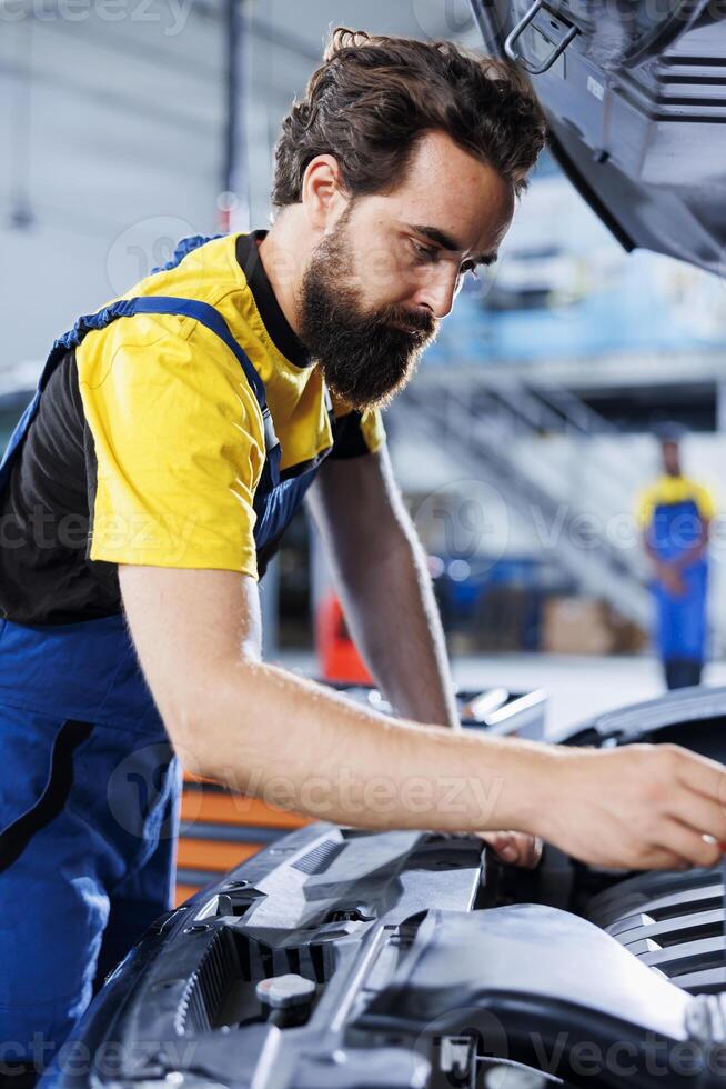 Car service mechanic expertly examines engine using advanced mechanical tools, ensuring optimal automotive performance and safety. Seasoned garage expert conducts annual vehicle checkup photo