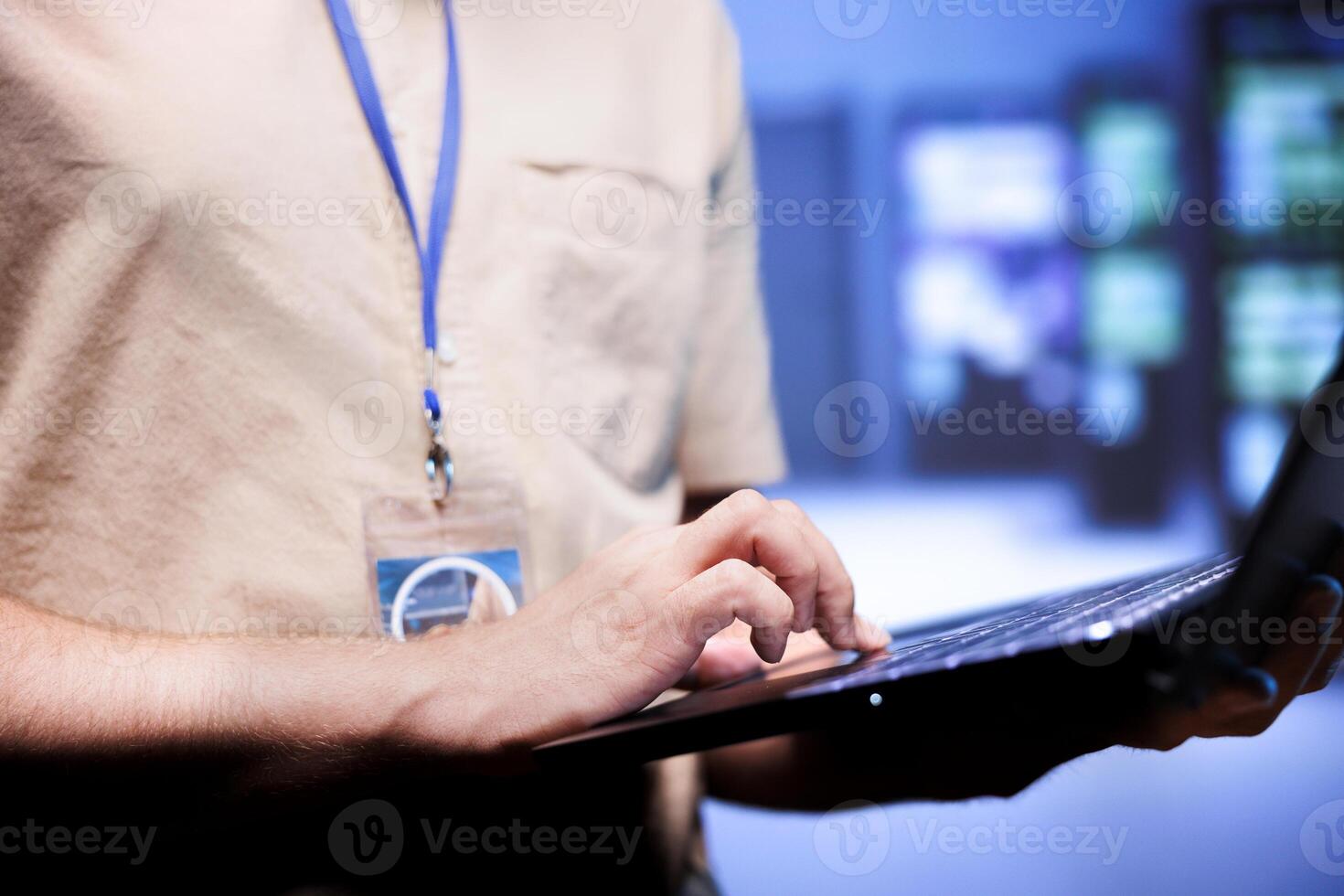 Worker in front of blurry background supercomputers delivering web content to online customers. Repairman in server room using laptop to make sure critical systems are working errorless, close up photo