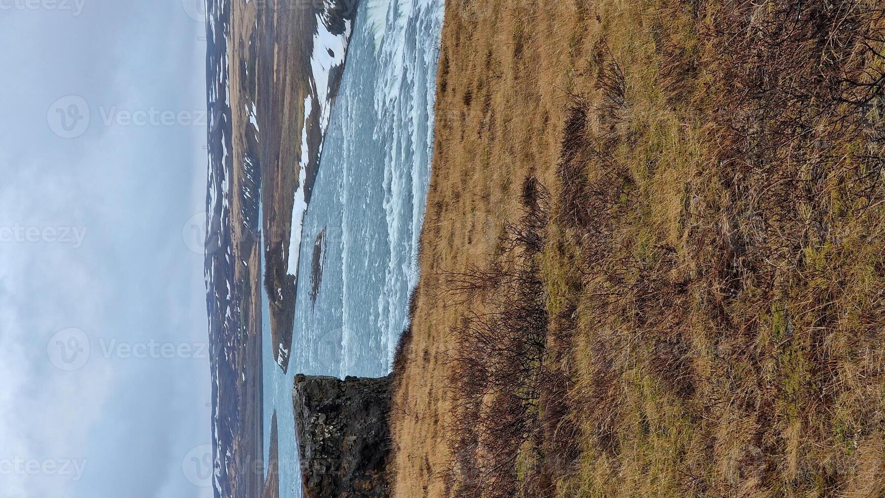 Gullfoss cascade in icelandic frosty region, fantastic nordic scenery with snow covered hills and freezing cold water falling off edge. River stream flowing on top of cliffs, natural waterfall. photo