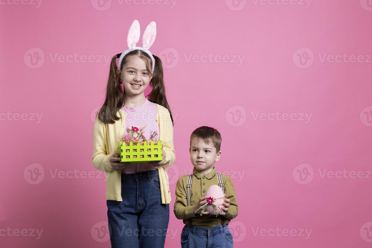 Small cute children showing easter ornaments and toys in studio, posing for a holiday celebration photoshoot. Little brother and sister siblings feeling excited about spring festivity and gifts. photo