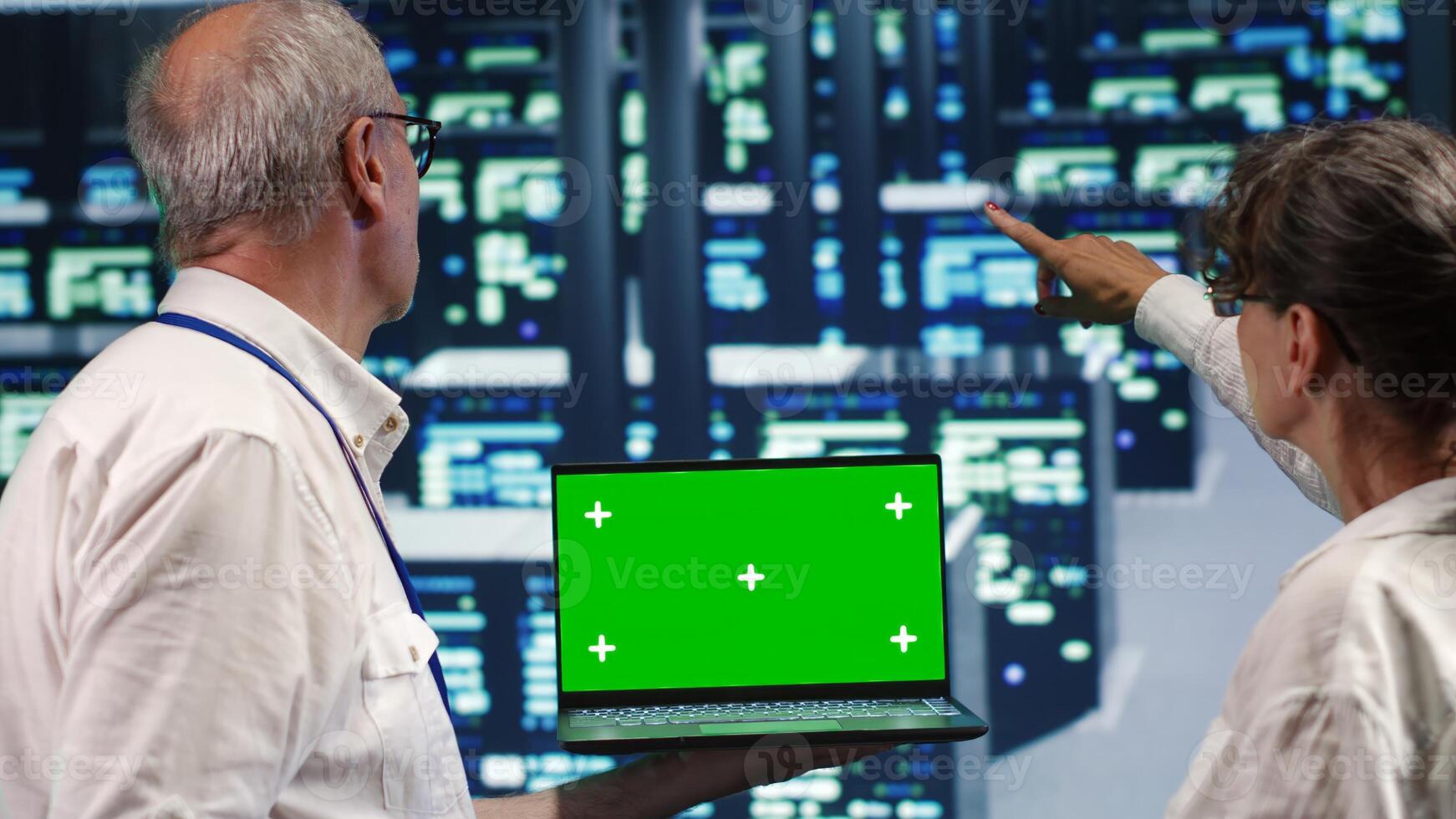 Meticulous experts looking around high tech data center, using mockup laptop to crosscheck disaster recovery plan and assess blade servers in need of replacement, preventing complications photo