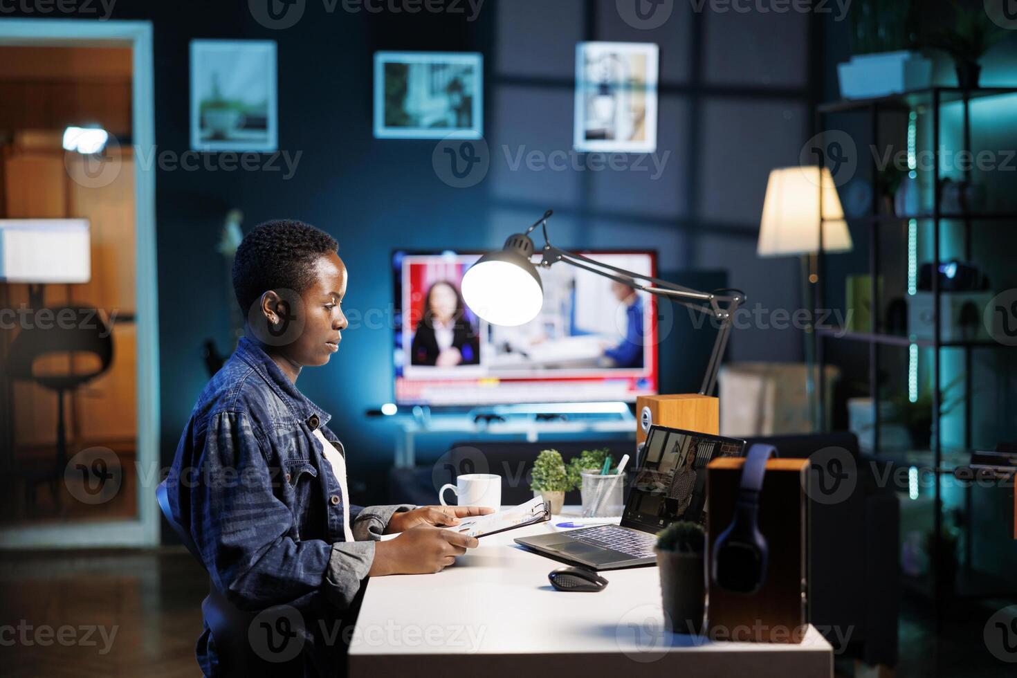 African american college student grasping paperwork while having a conversation through a laptop with female colleague. Two young women having an online discussion, video call on portable computer. photo