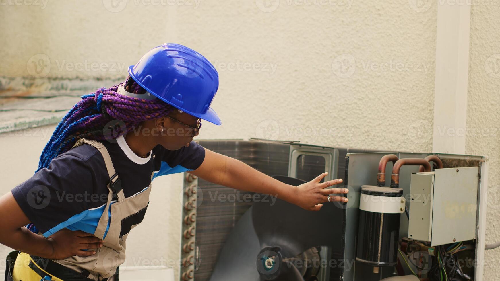 African american worker contracted to repair broken air conditioner, testing faulty blower fan slowed down by dirt. Wireman investigating opened hvac system to check for improper wiring photo