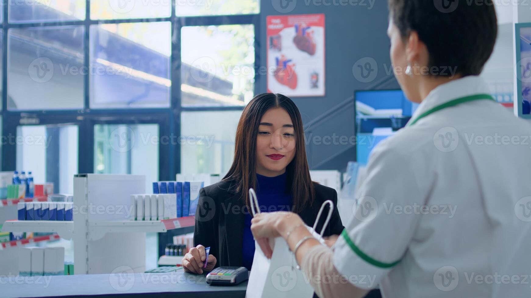 Asian woman in drugstore at checkout counter using credit card to purchase medical items. Happy customer doing contactless paying in pharmacy after finding needed virus stopping pills photo