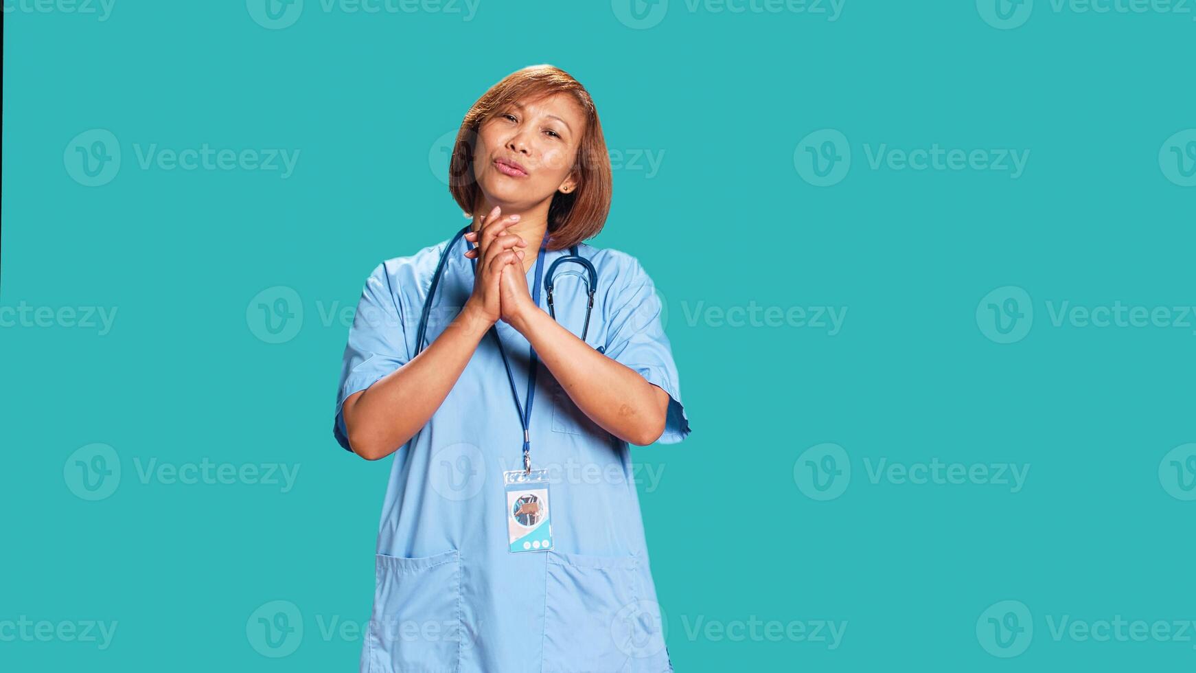 Pleading asian healthcare professional imploring hospital management for wage raise. Overworked nurse with hands folded in prayer gesture asking for days off, isolated over blue studio background photo