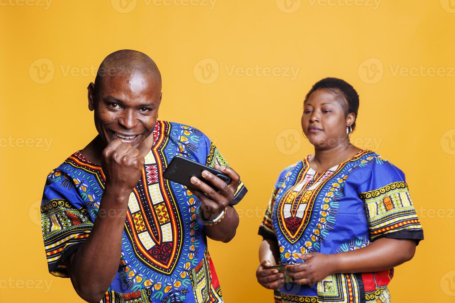 Excited man winning mobile game on smartphone while participating competition with girlfriend. Black couple wearing ethnic clothes enjoying videogame on smartphone and husband showing winner gesture photo