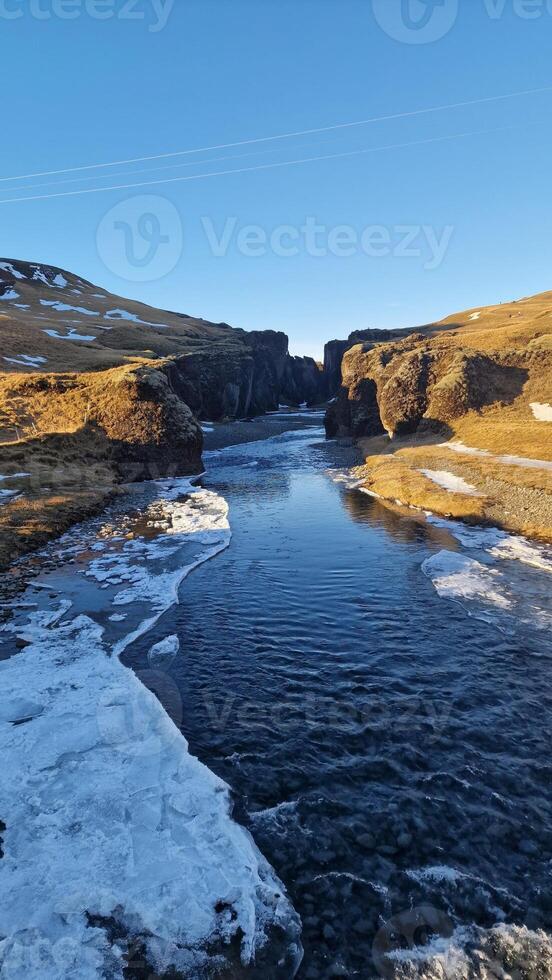 Snowy icelandic canyon with frozen water stream and cliffs covered in frost creating gorgeous landscape view. Magical fjadrargljufur canyon with river flow in iceland between slopes. photo