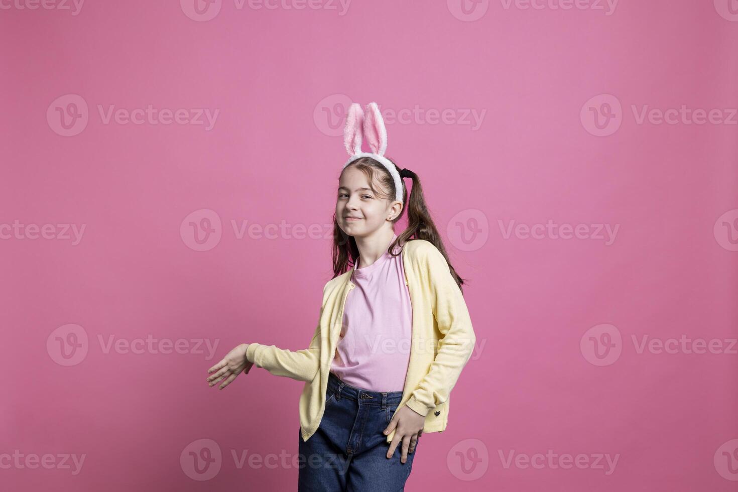 Joyful toddler with pigtails and bunny ears dancing on camera, showing cute dance moves and fooling around in studio. Sweet young girl feeling excited about easter celebration event. photo