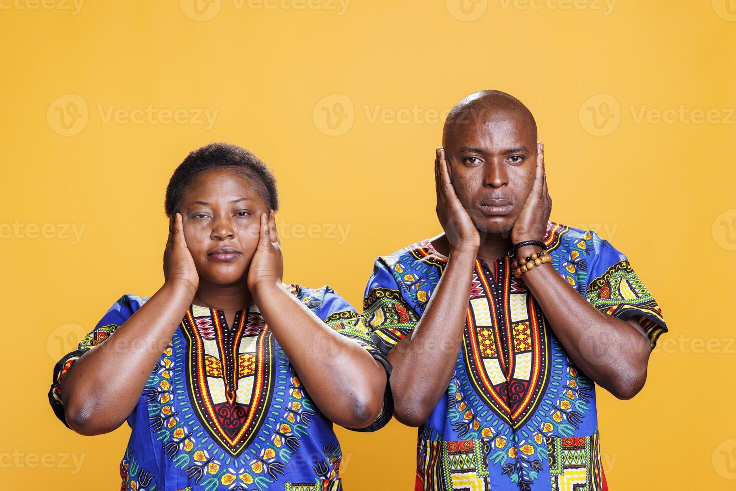 African american couple covering ears with hands, showing hear no evil three wise monkeys portrait. Man and woman ignoring loud noise and looking at camera on studio background photo