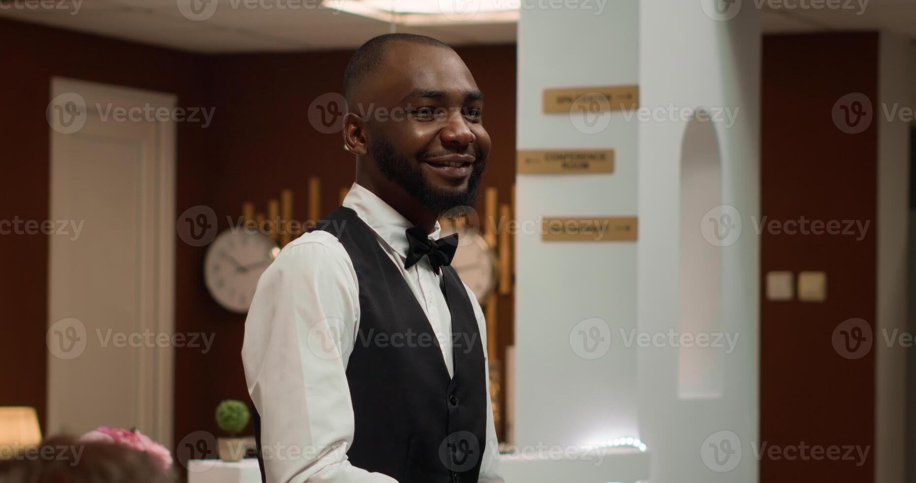 hotel conserje ofrecimiento servicios a invitado y ayuda con carretilla bolsas, Proporcionar excelente asistencia en salón zona vestíbulo. africano americano frente escritorio personal que lleva equipaje. Mano disparo. foto