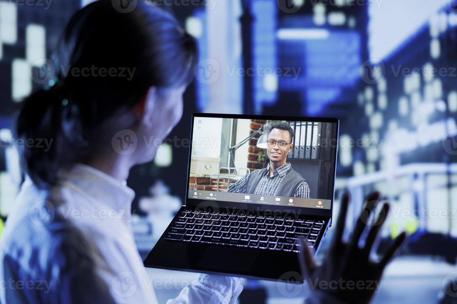 Asian man in videocall with coworker while strolling around city streets at night, giving him work updates. Person using laptop to show colleague surroundings in nighttime urban environment photo