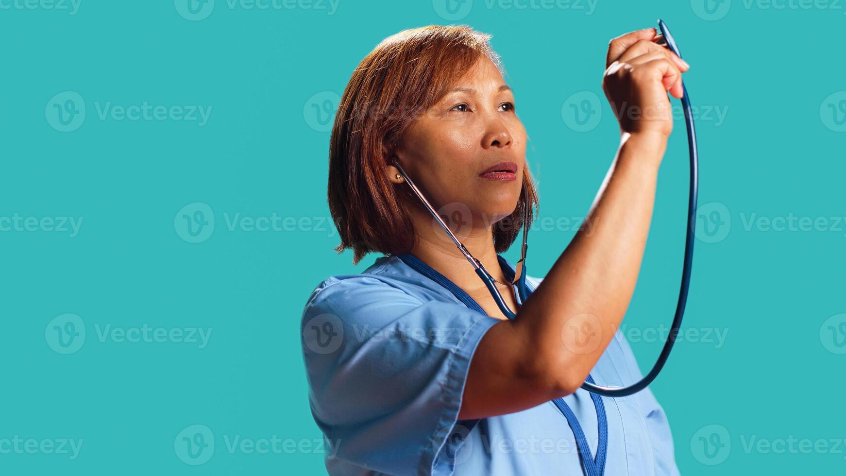 Certified BIPOC hospital worker using stethoscope, measuring vital signs. Close up shot of nurse isolated over studio background utilizing professional medical device to provide diagnostic photo