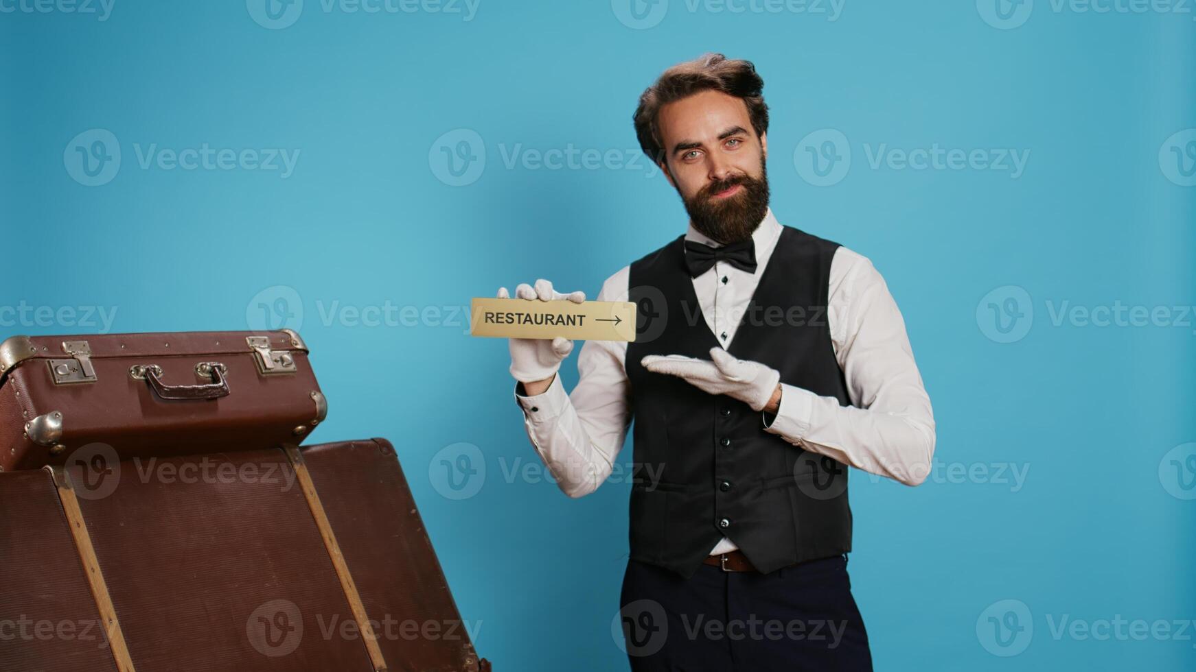 Hotel porter advertises restaurant sign to help travellers with premises directions, holding diner pointer while he wears white gloves. Bellhop pointing at symbol for the dining space. photo