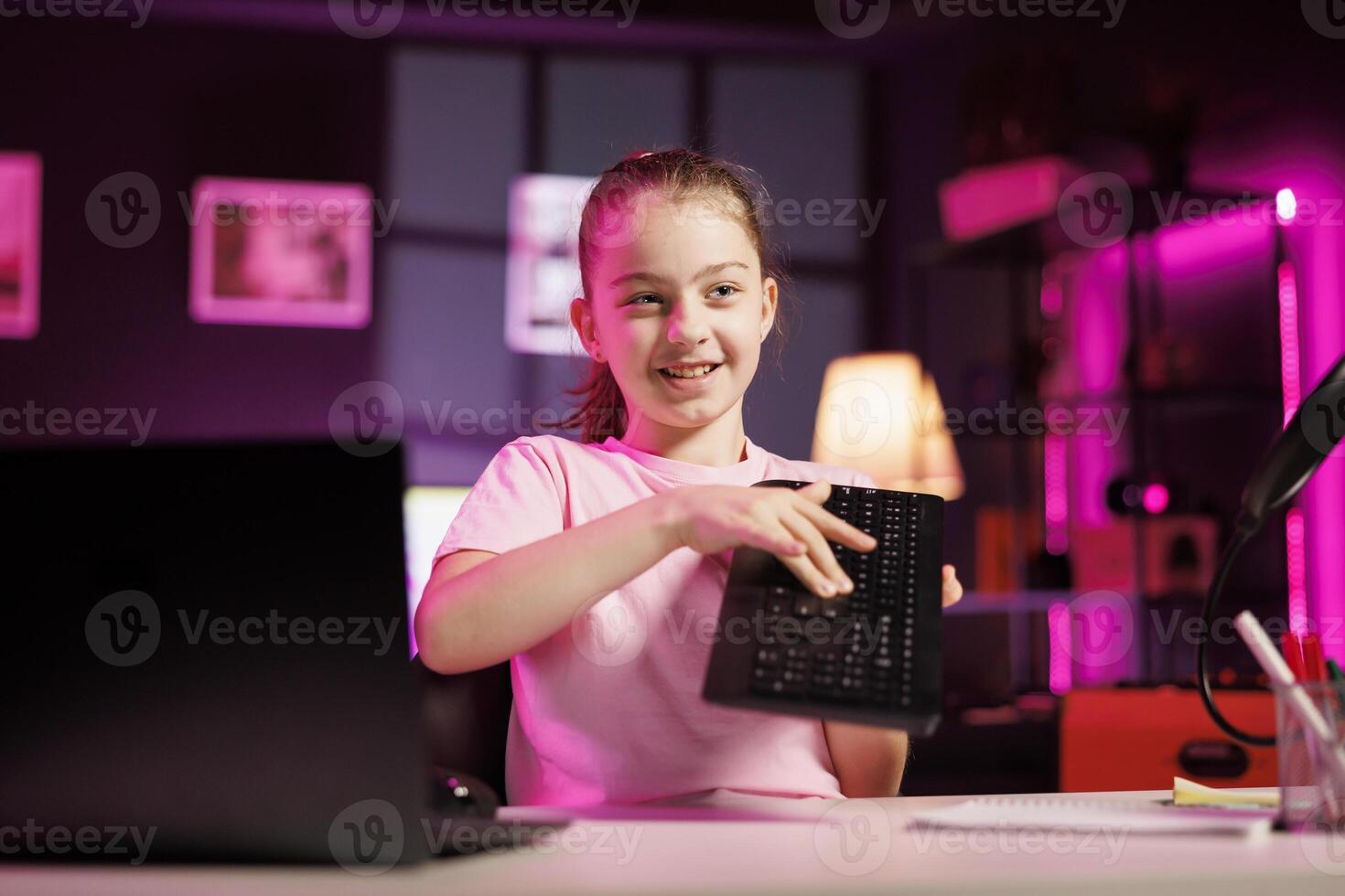 Child influencer filming wireless mechanical keyboard review in studio, showing capabilities and specifications. Little girl clicking keys on gaming computer peripheral, testing durability photo