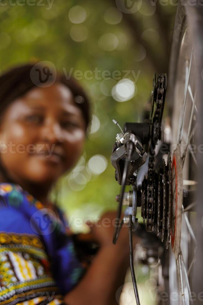Image showing close-up view of bike chain ring crank and barrel adjuster being inspected and adjusted outdoor by african american female. Detailed shot of bicycle cassette. photo