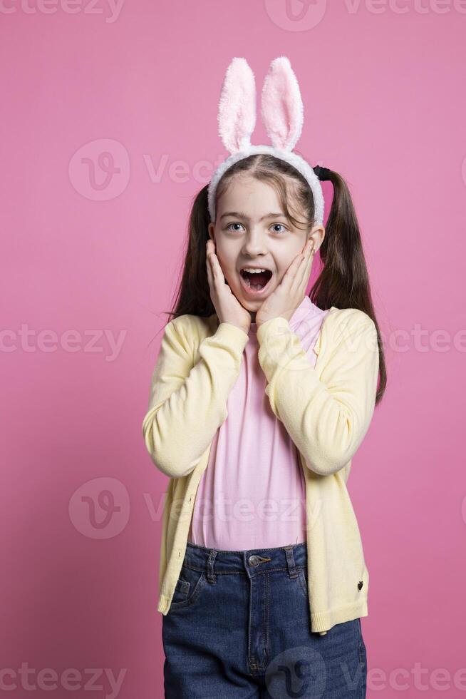 Enthusiastic positive kid acting surprised by easter gifts in studio, feeling cheerful with her presents and enjoying april festivity. Young optimistic child getting excited about spring celebration. photo