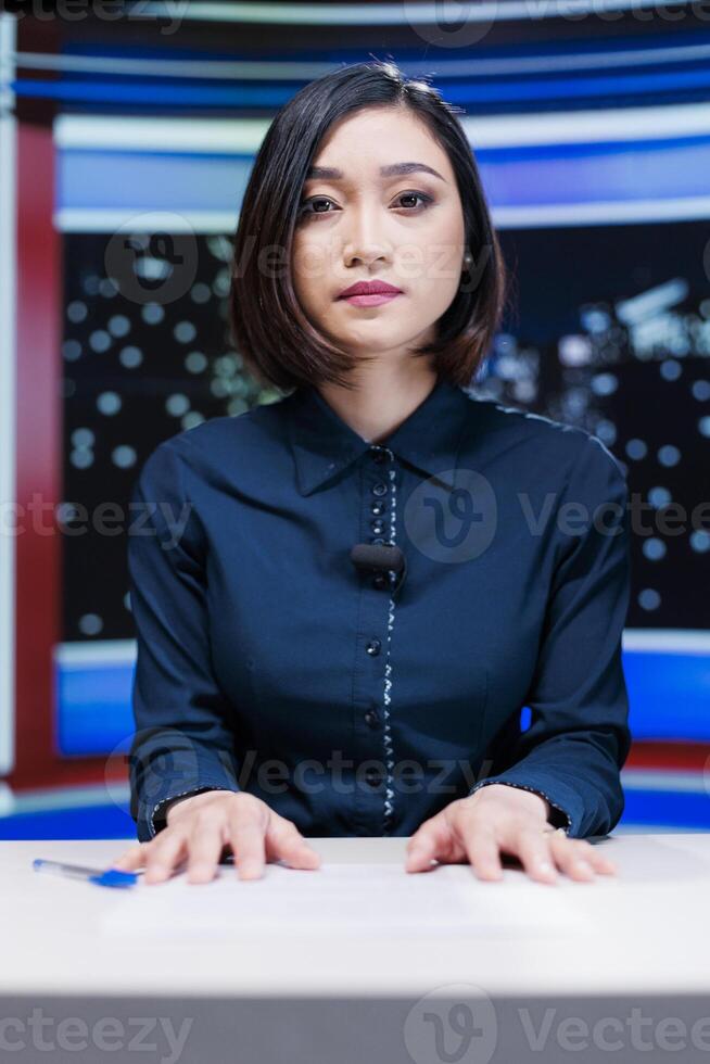 Presenter on midnight news show addressing media outlets information about international events during live segment. Asian woman talking about international newscast with details. photo