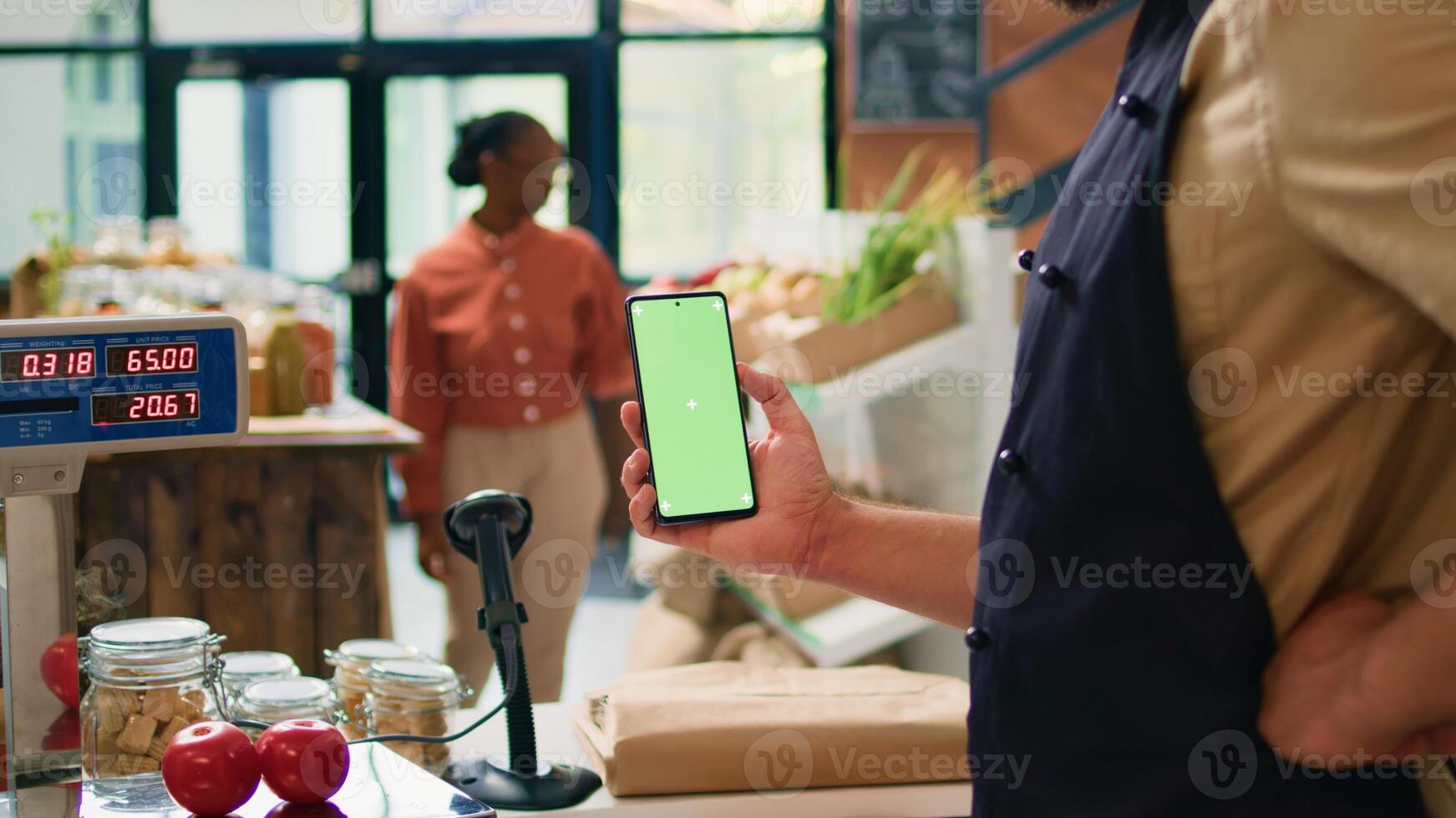 Young man holds smartphone at store checkout, presenting isolated greenscreen display on mobile device. Farmer and vendor using blank chromakey template with copyspace technology. photo