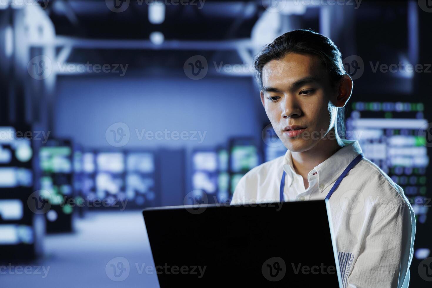 Skilled programmer in data center uses laptop to prevent system overload during peak traffic periods. Experienced professional in server room ensuring enough network bandwidth for smooth operations photo