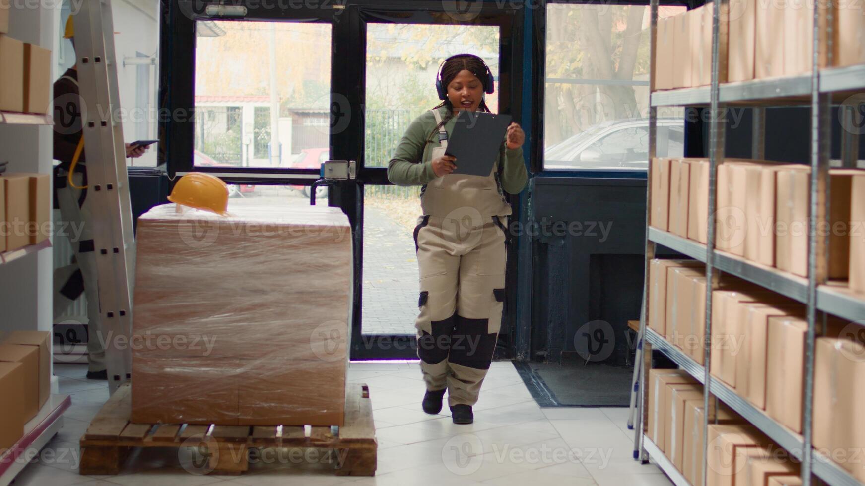 Happy warehouse sorter listening music enjoying herself while checking labels on cardboard boxes. Cheerful worker wearing heaphones and dancing around while walking through storage room rows photo