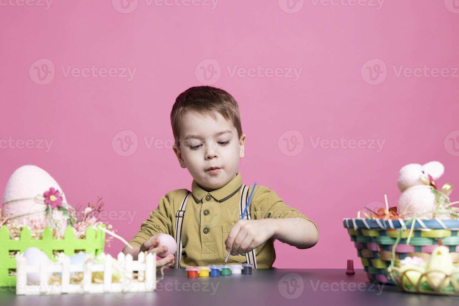 Delighted young kid coloring eggs and ornaments with watercolors as he prepares artistic creations for Easter Sunday festivities. Playful toddler having fun in the studio with tie dye painting. photo