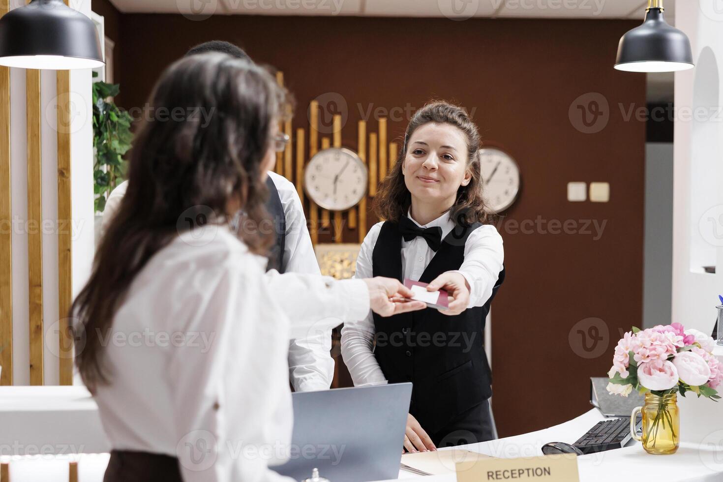 hembra conserje ansiosamente da la bienvenida y ayuda mayor viajero, cheques identificación para sin costura registrarse. a frente escritorio, hotel recepcionista devoluciones pasaporte a mayor mujer después verificación. foto