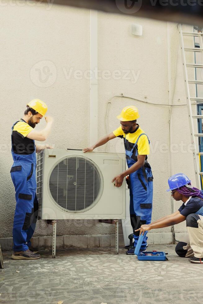 Trained professionals installing condenser for home owner. Qualified technicians commissioned to optimize new HVAC system's performance, ensuring it operates at maximum efficiency photo