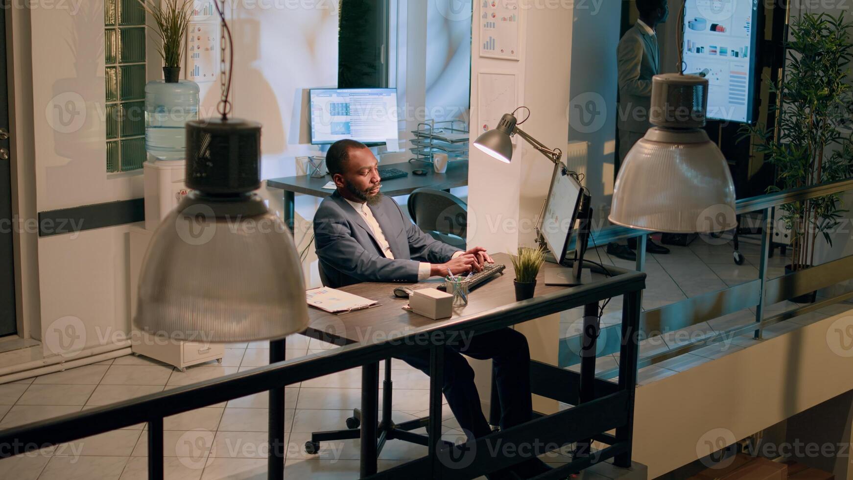 Jib down shot of african american bookkeepers sitting at desk, looking over accounting figures, imputing data on computer during nightshift. Meticulous business team solving tasks before deadline photo