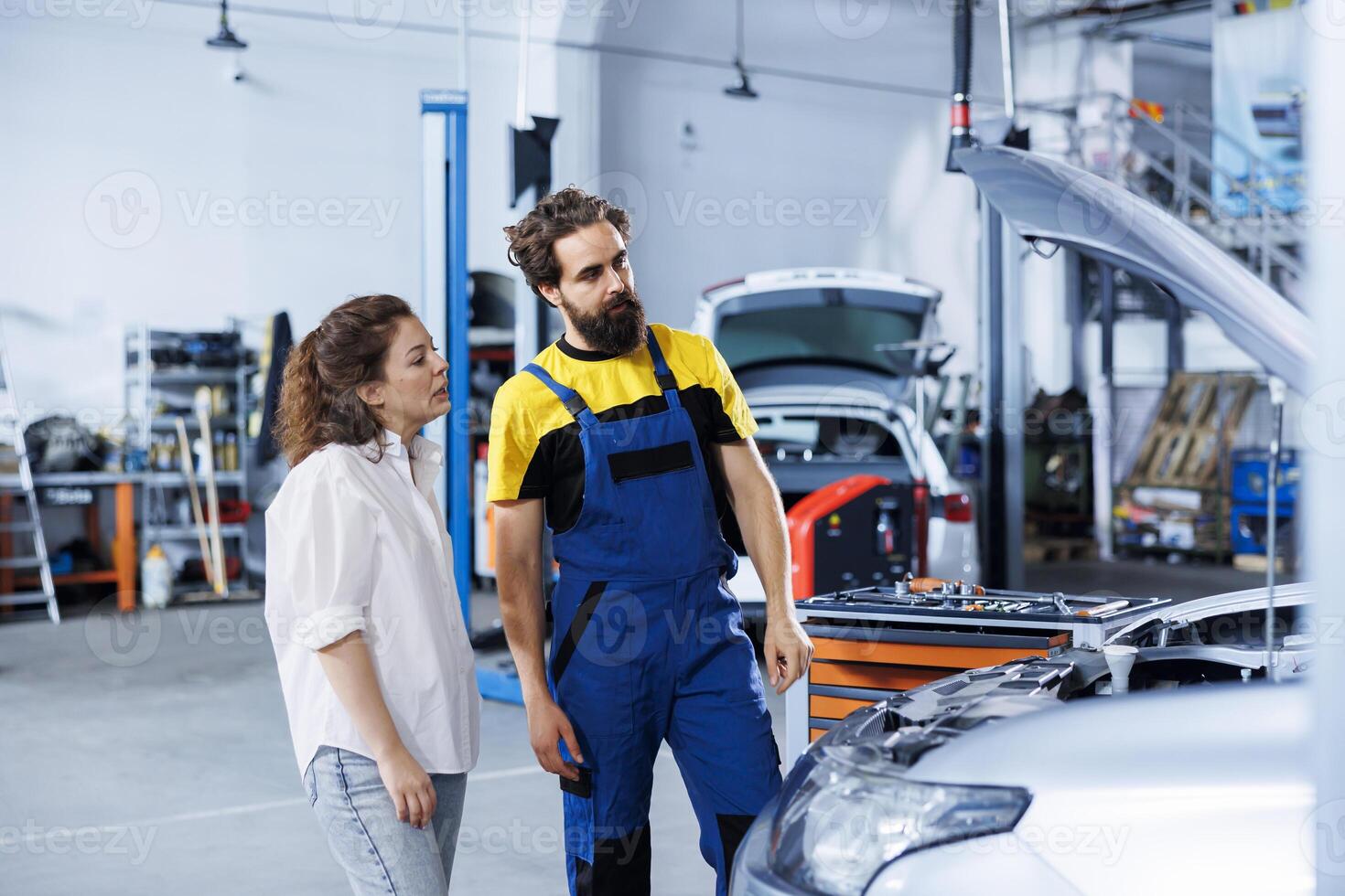 Mechanic at auto repair shop conducts annual vehicle checkup, informing customer about needed ignition system replacement. Qualified garage employee talks with customer after finishing car inspection photo