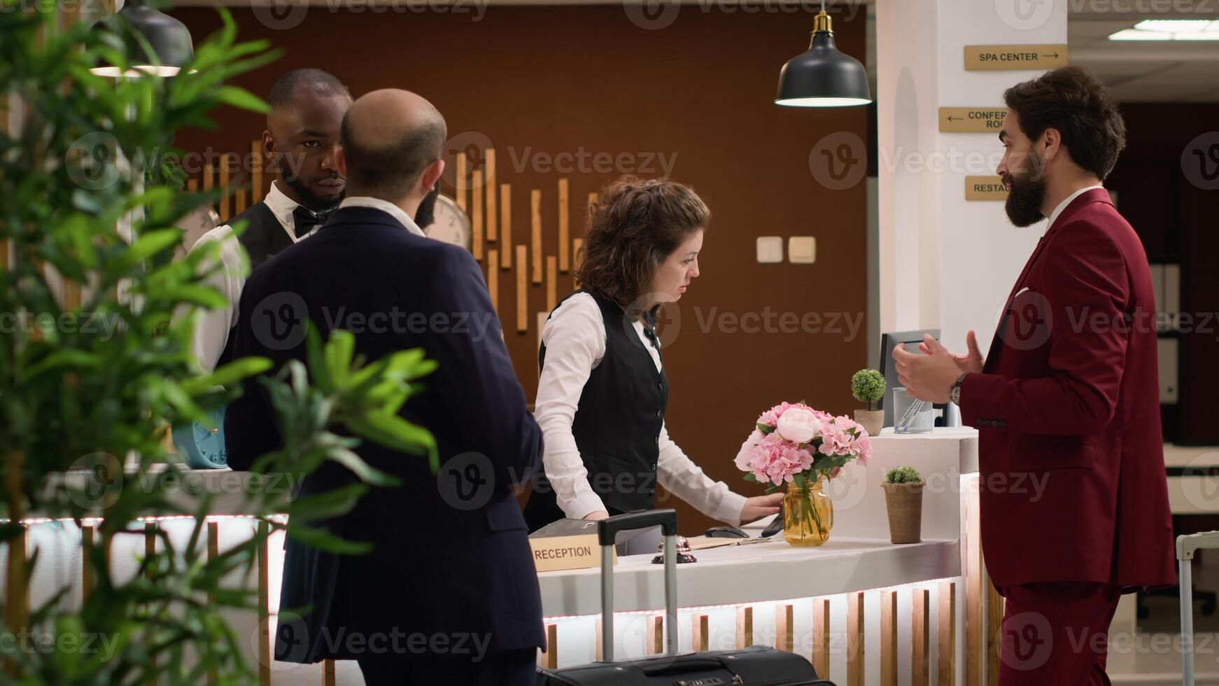 Business people enter hotel reception, talking to woman employee and to fill in check in papers. Two entrepreneurs registering at resort to prepare for upcoming official meeting, work trip. photo