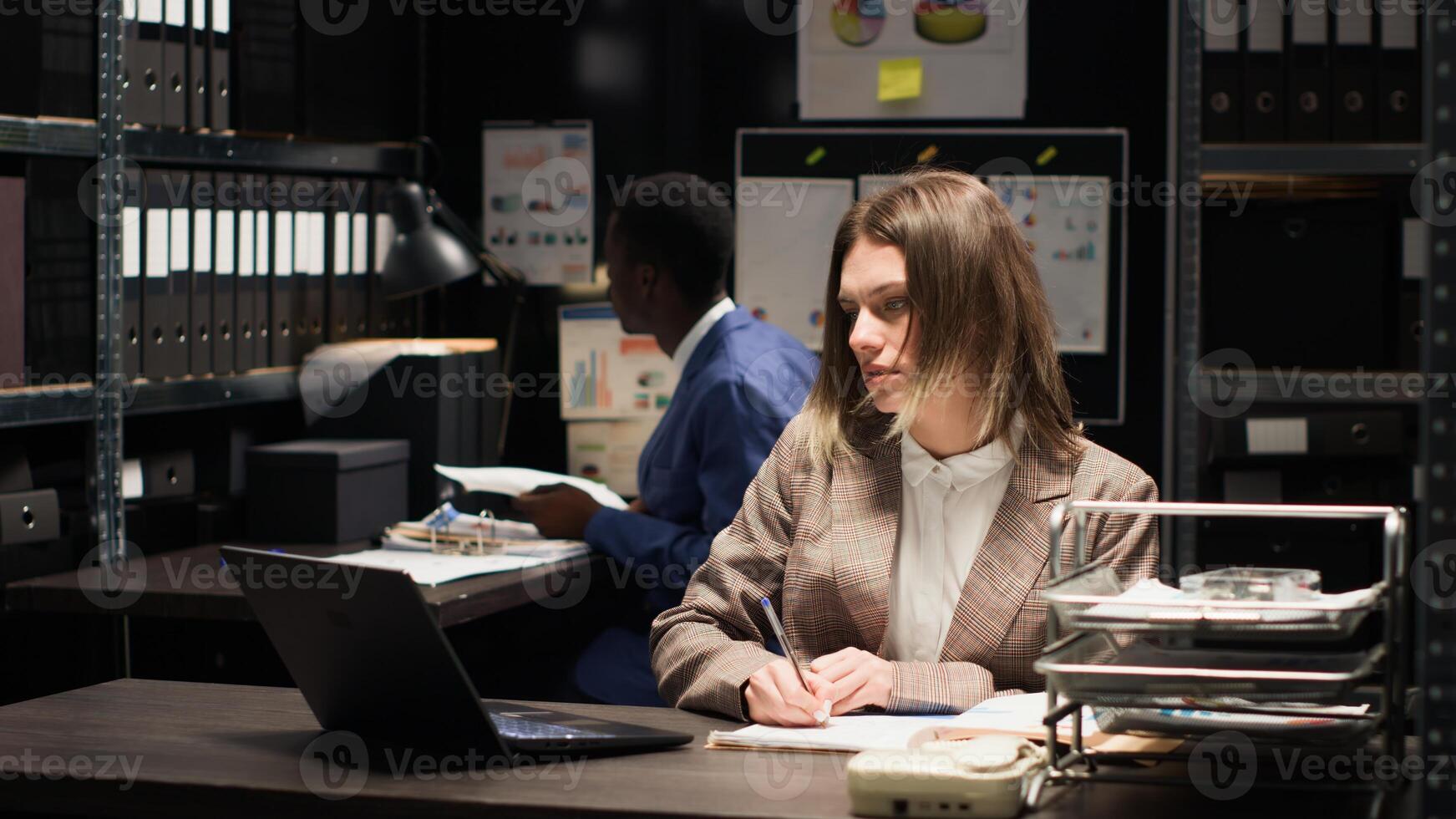 Caucasian detective inspector arrives for investigation with files, photos, and papers organized for research and surveillance. Female private detective examines records with expertise using laptop. photo
