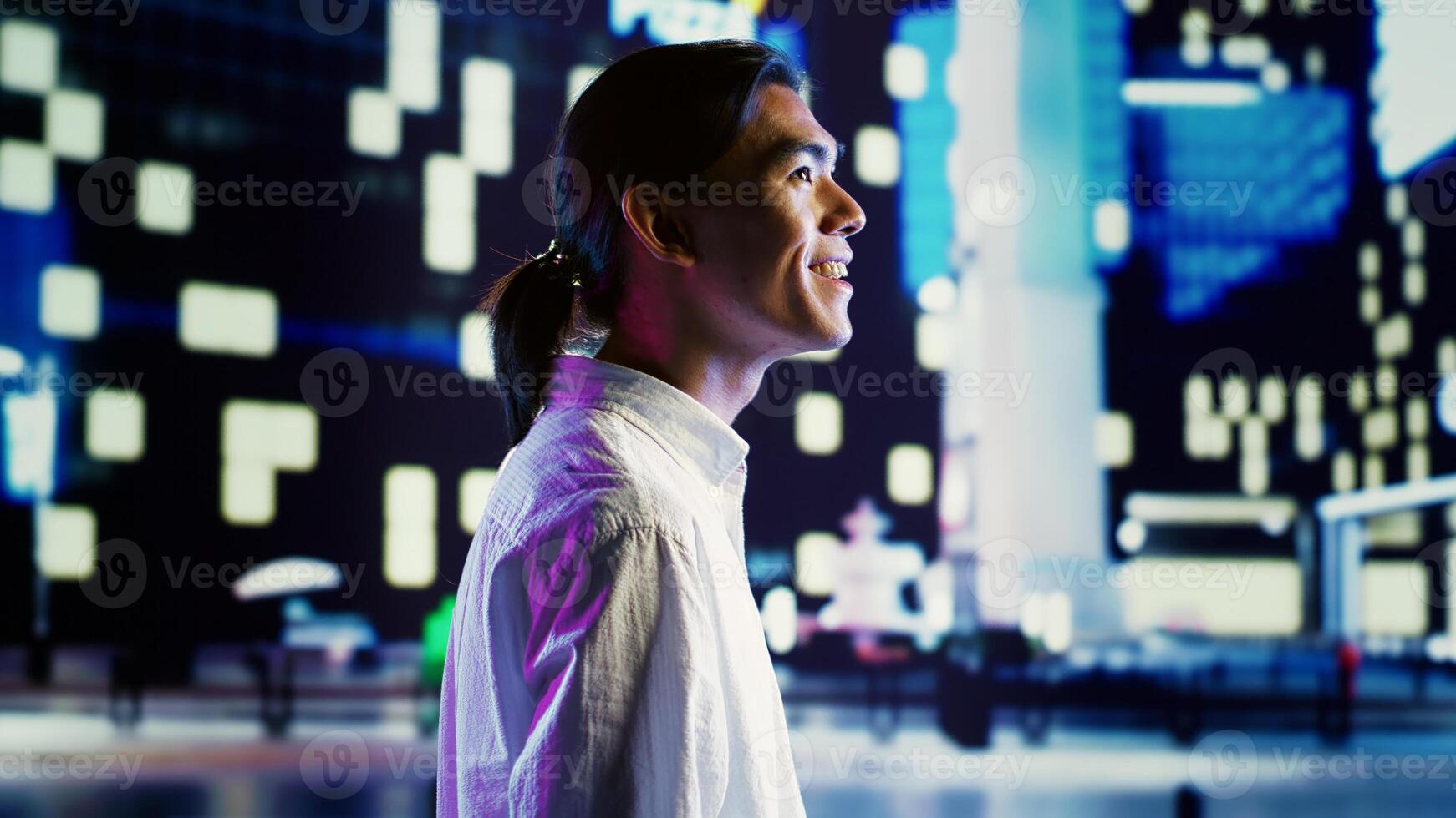Asian man wandering around city streets at night, looking upwards to surrounding condominiums in empty urban center with no traffic. Cheerful businessman taking a walk to clear his mind photo