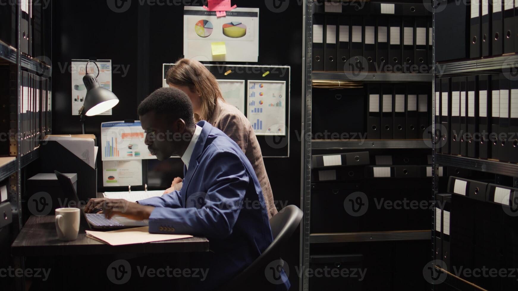 In office, two private investigators are analyzing forensic evidence on laptop and discussing illegal information. Policeman drinks coffee while female cop provides crucial information. Aerial shot. photo
