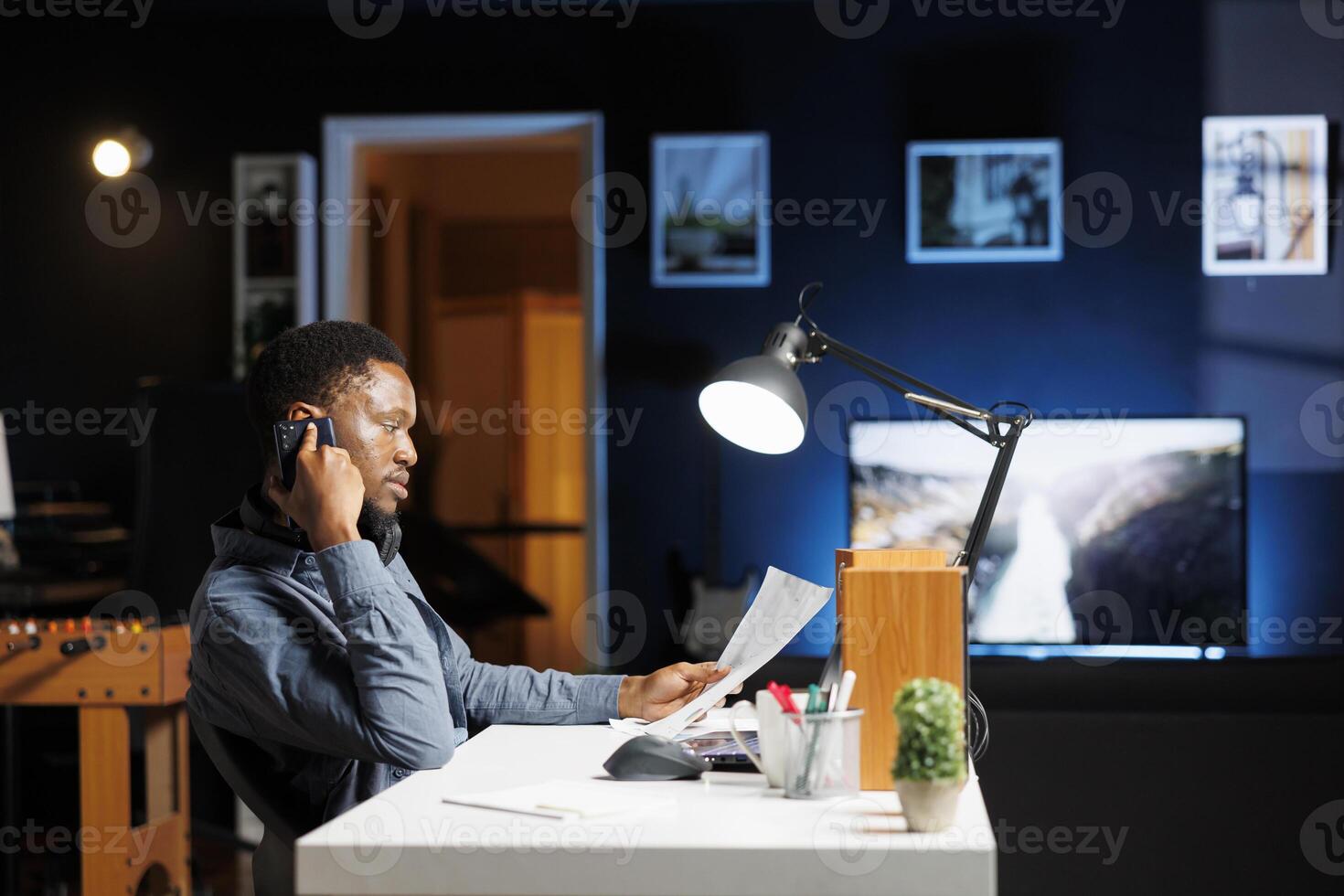 African american man calling investors to obtain new funds for capital investment, working from home to develop business on global market. Young employee chatting on phone call at night. photo