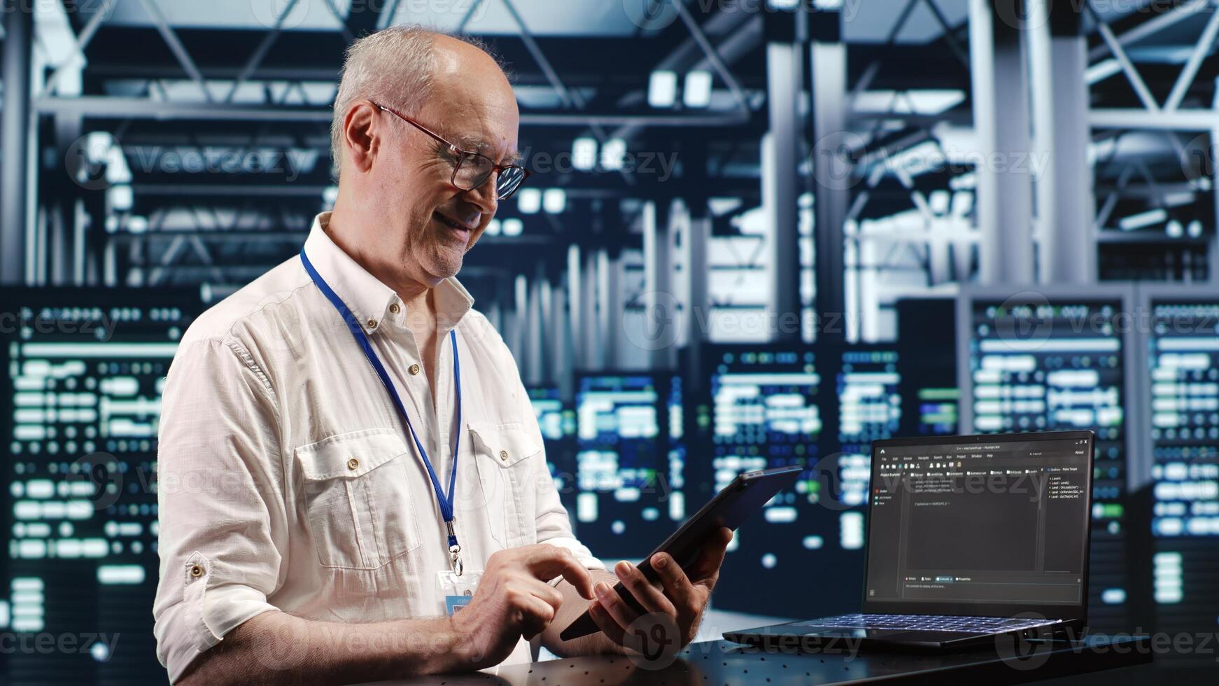 Old system administrator in data center, solving tasks on tablet while running scripts on laptop terminal. Qualified employee amidst servers, accessing databases and manipulating lines of code photo