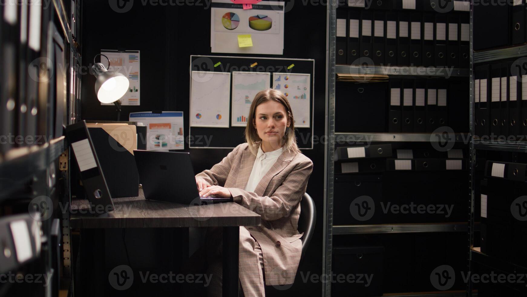Confident female private detective investigator reviews clues in office, searching on laptop for evidence to solve crime. Profile portrait of focused caucasian policewoman using personal computer. photo