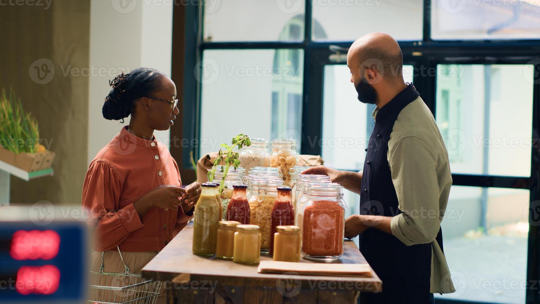 propietario recomienda abultar productos para mujer, presentación variedad de productos quimicos gratis granos y Cocinando ingredientes almacenado en reutilizable frascos. Encargado de tienda explica ecológico producción proceso a cliente. foto