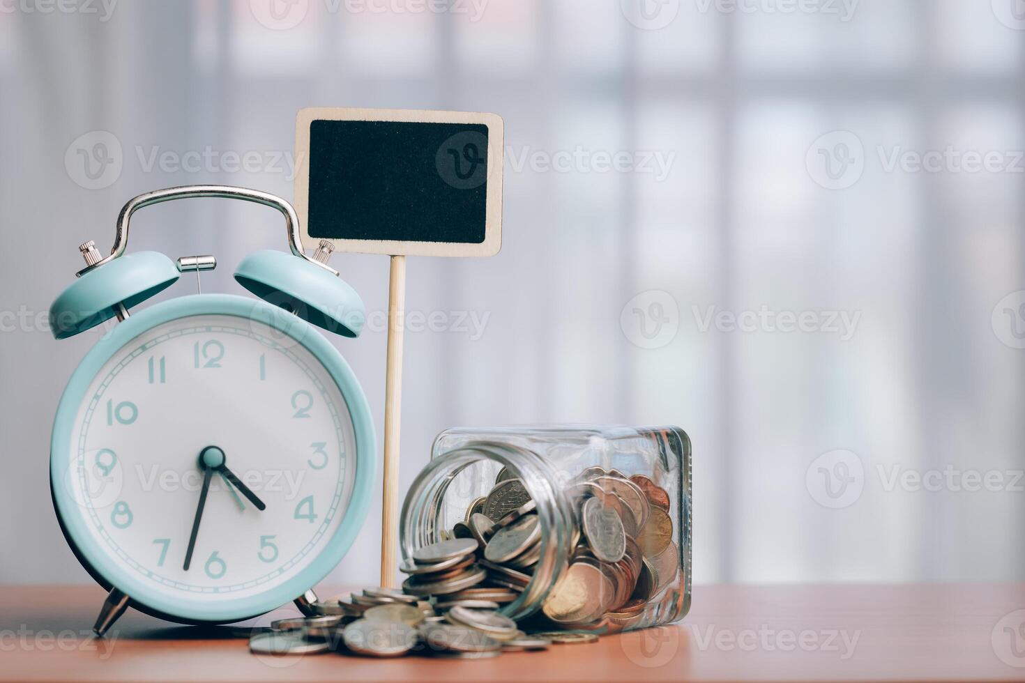 Alarm clock and coins with blank chalkboard on wood table with copy space photo