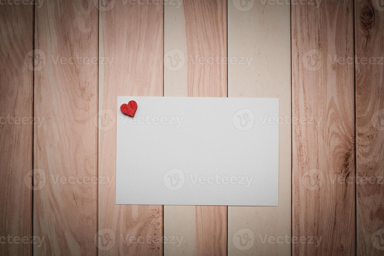un blanco papel con un rojo corazón metido en un de madera mesa foto
