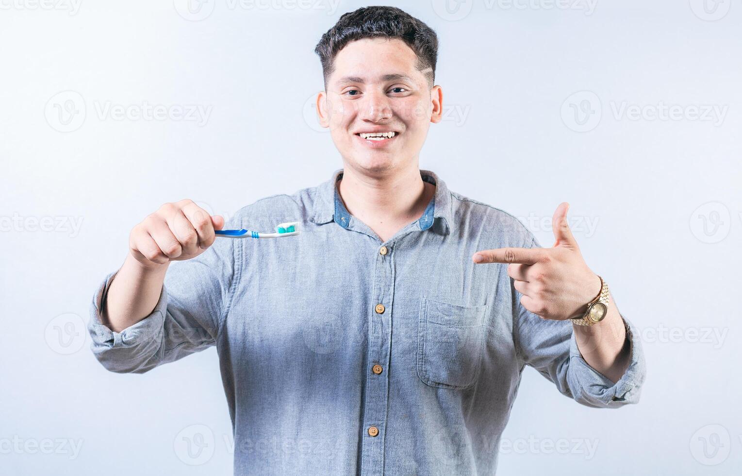 Man holding and recommending a toothbrush. Smiling guy holding and pointing at toothbrush isolated. Happy person showing and pointing at toothbrush photo
