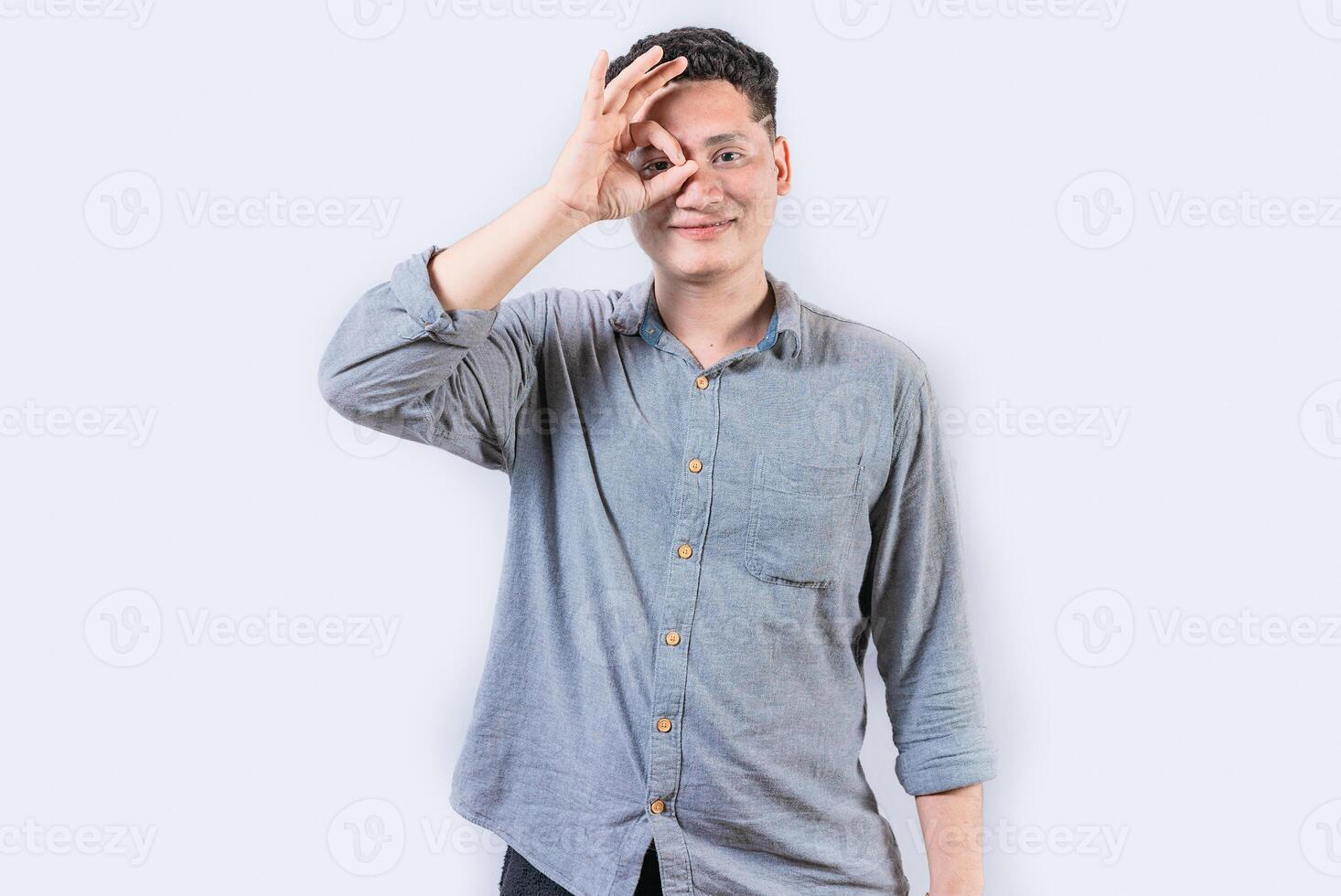 Happy young man making ok gesture with hand looking through fingers. Smiling person making ok gesture looking through fingers isolated photo