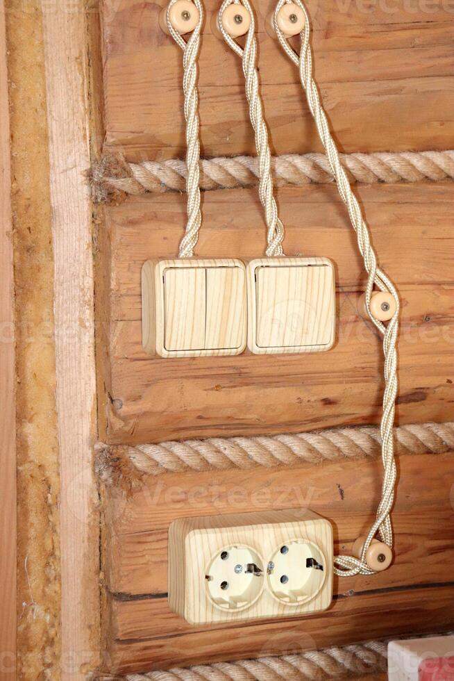 Electric switches, retro wires and sockets in a country house on a log wall in the hallway. Vertical photo, close-up photo