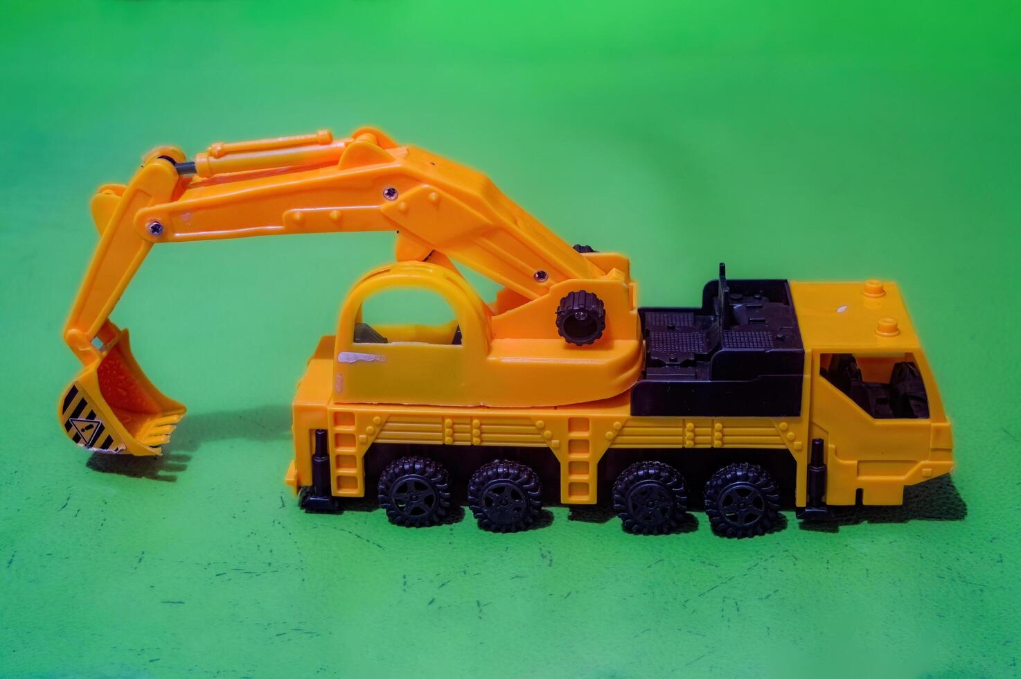 a yellow toy miniature excavator on a flat green background photo